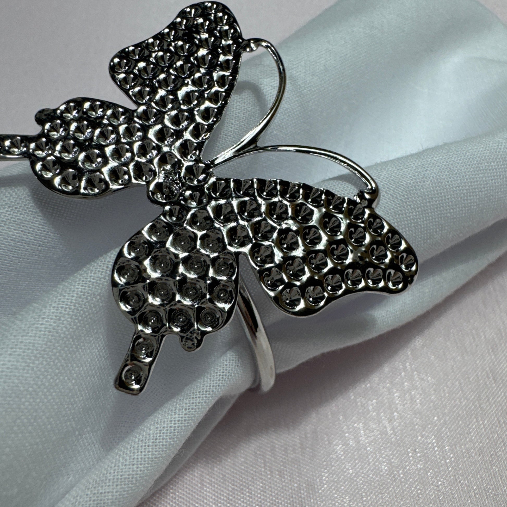 Set of 6 silver butterfly napkin rings displayed on cloth napkin and dish.


