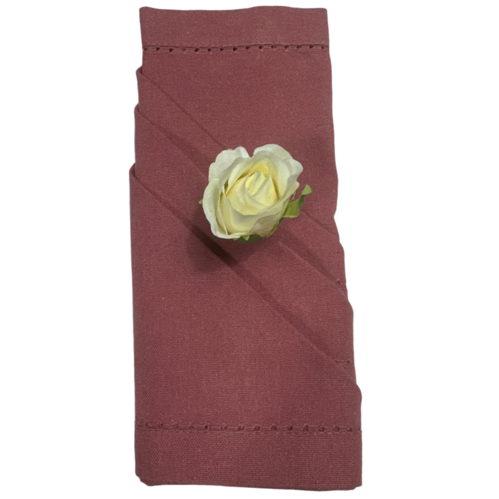 A folded cotton napkin in a warm rose color with a diagonal fold and a small artificial white rose accent on top, featuring delicate hemstitching along the edges
