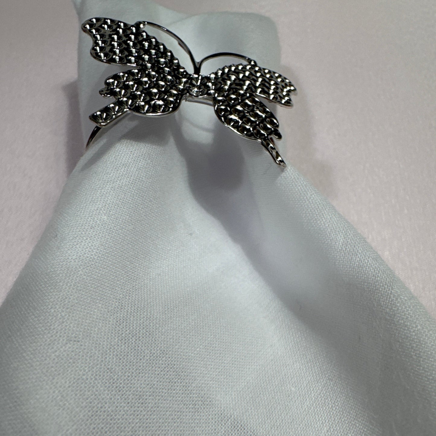 Set of 6 silver butterfly napkin rings displayed on cloth napkin and dish.

