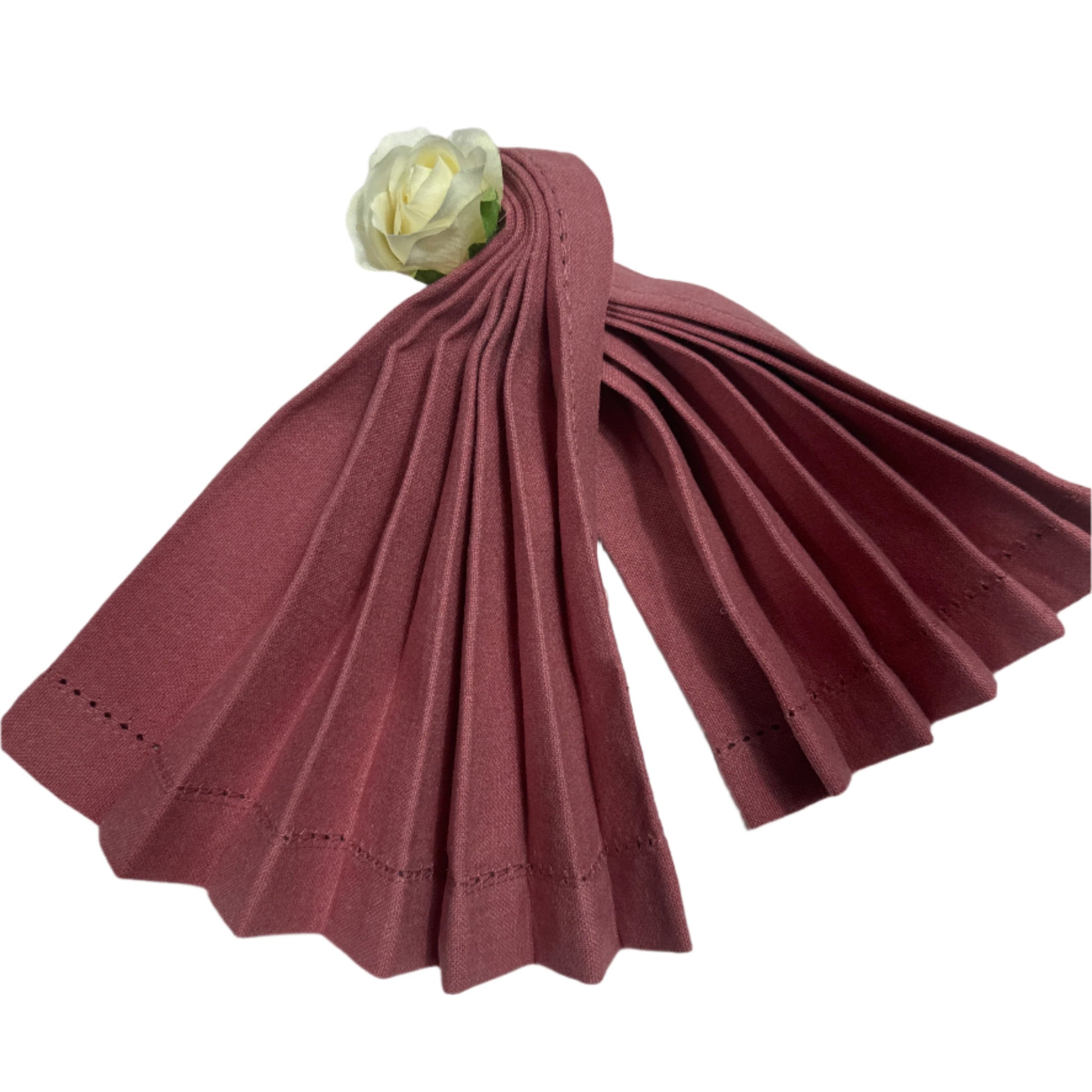 A set of pre-folded cotton napkins in a rich burgundy color, showcasing pleated edges with fine stitching. A delicate white rose is placed at the top, adding a touch of elegance to the neatly arranged napkins
