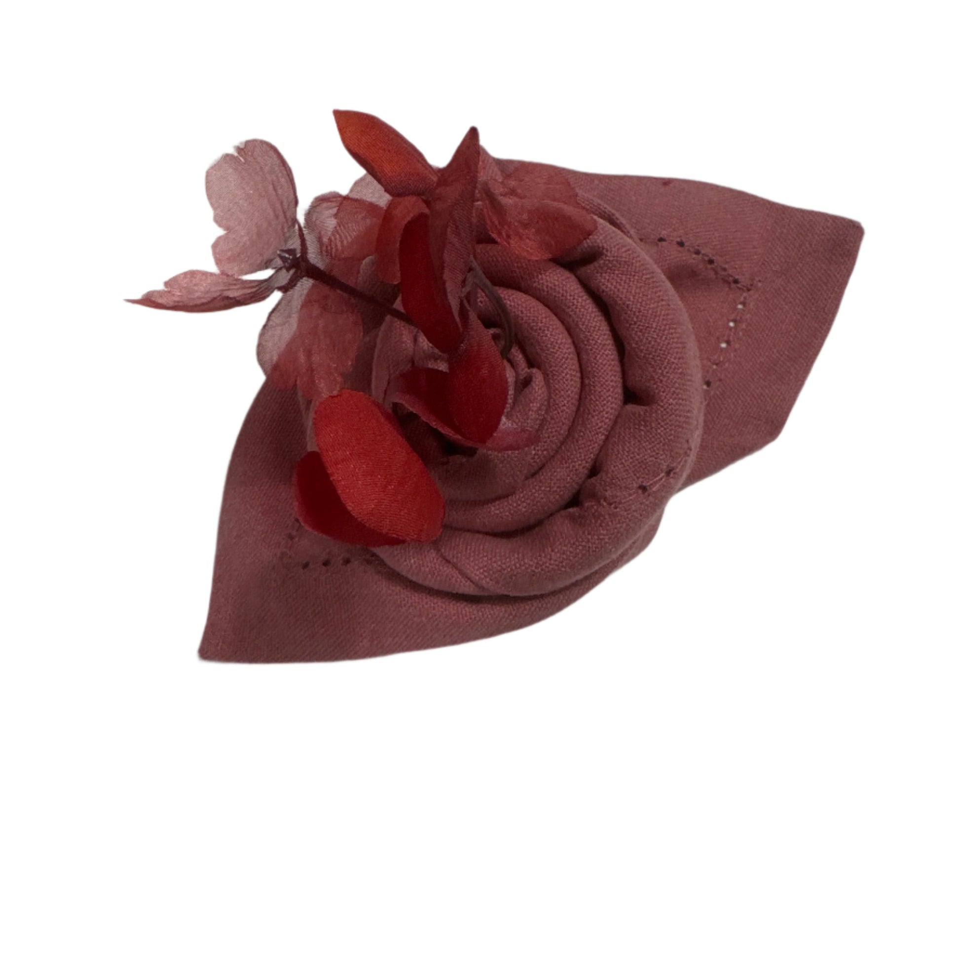 A rolled cotton napkin in rose color, adorned with delicate red fabric flowers, highlighting the hemstitch detailing along the edges